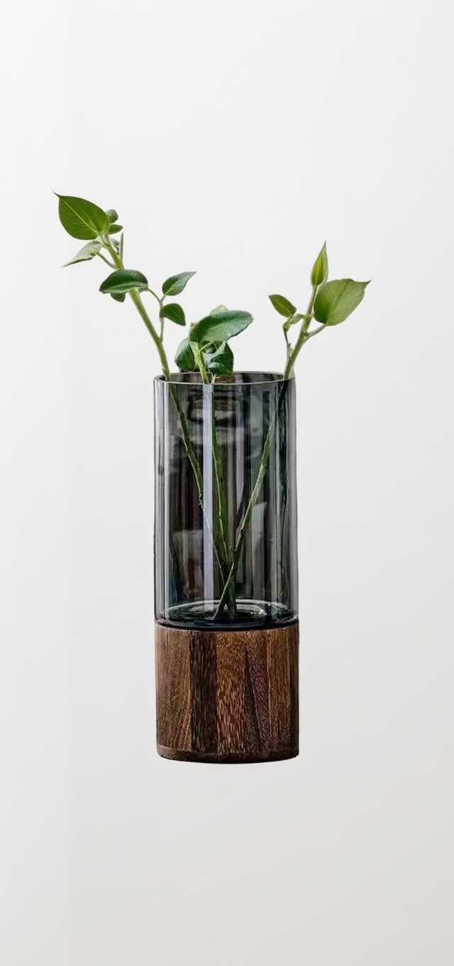 Glass vase with wooden base holding a plant on a table