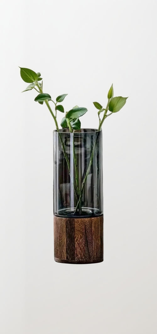 Glass vase with wooden base holding a plant on a table